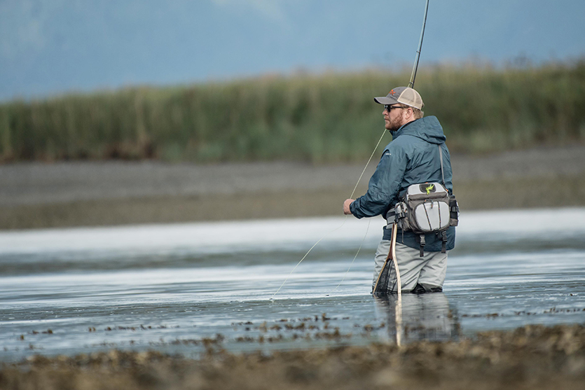 man with a beard wearing waders in a lake surrounded by grass